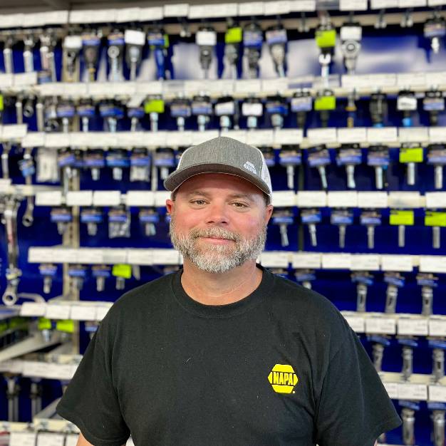 Man smiling in front of a wall of keys in a hardware store.