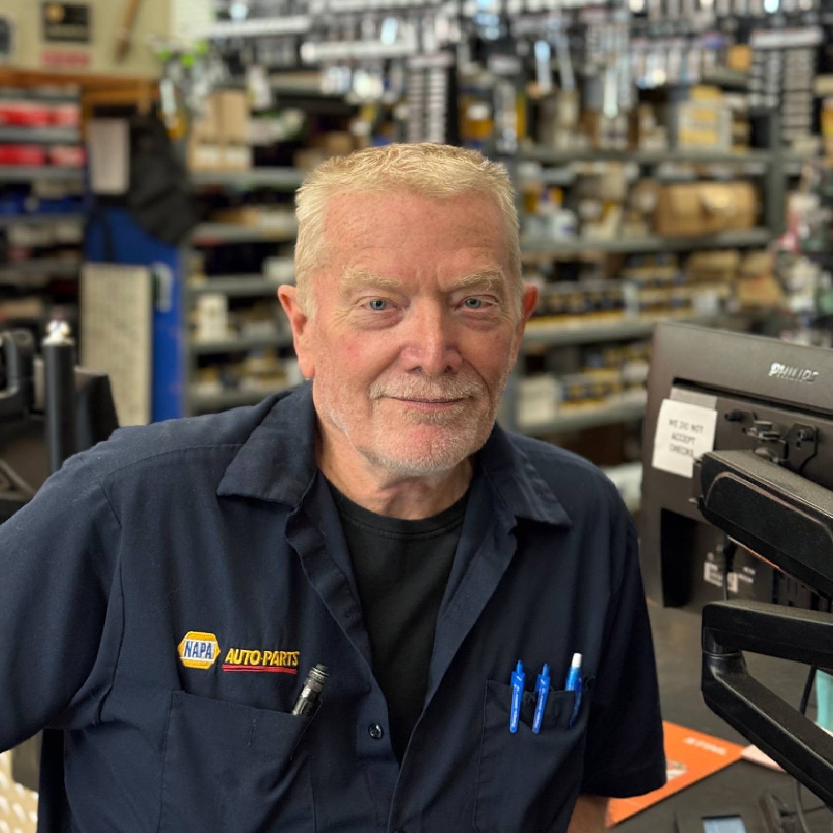 Smiling older man in a workshop or hardware store environment.