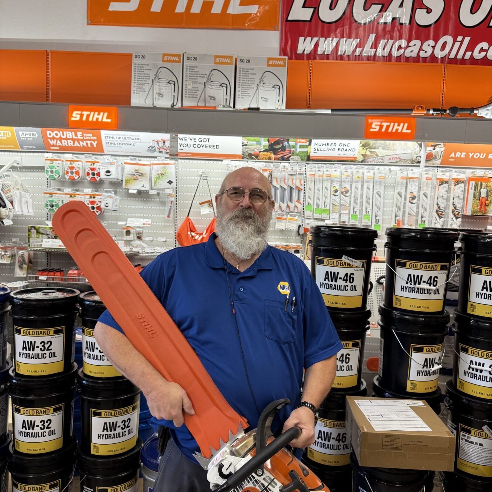 Man with a beard holding a large orange chainsaw in a hardware store.