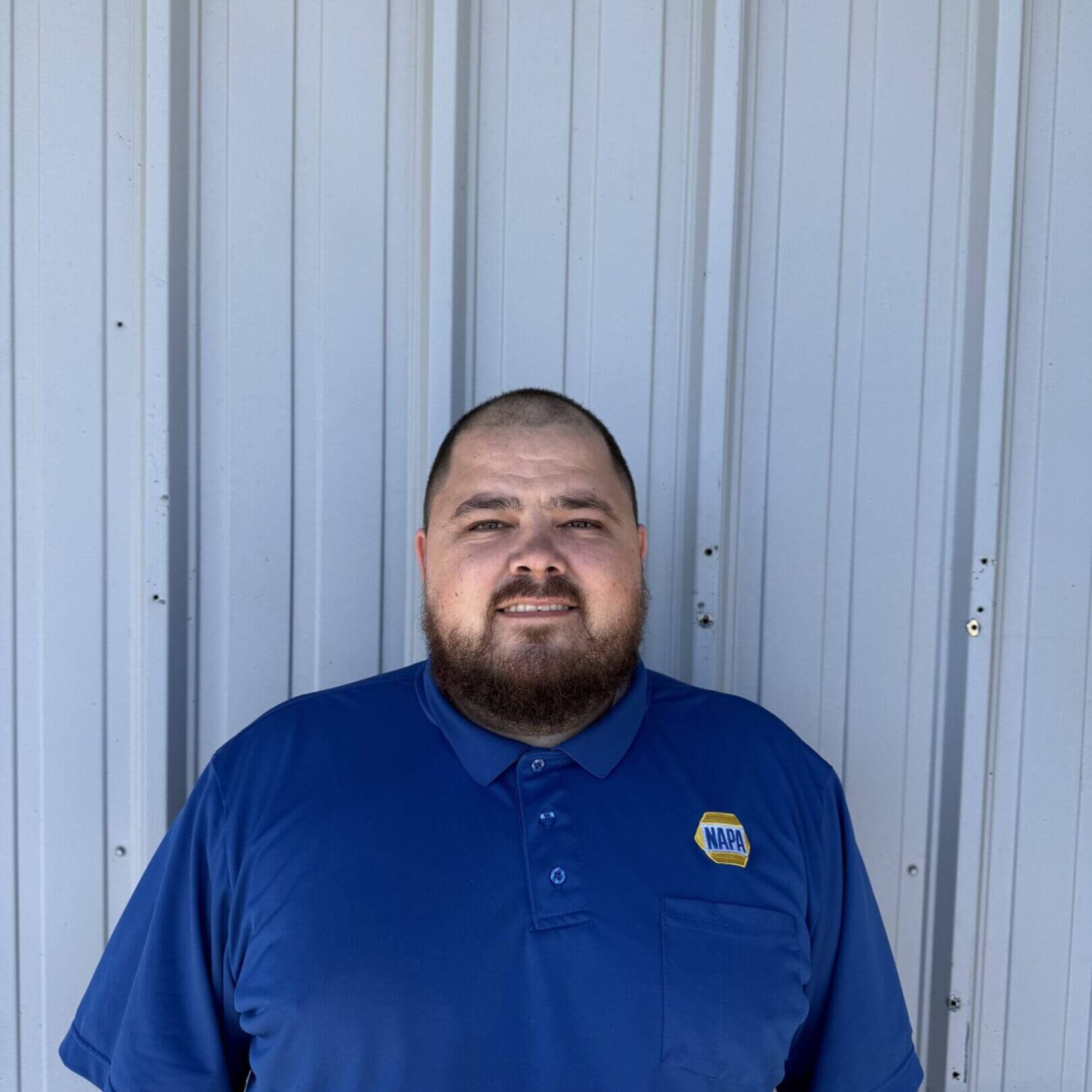 Man in a blue polo shirt smiling against a metal wall.