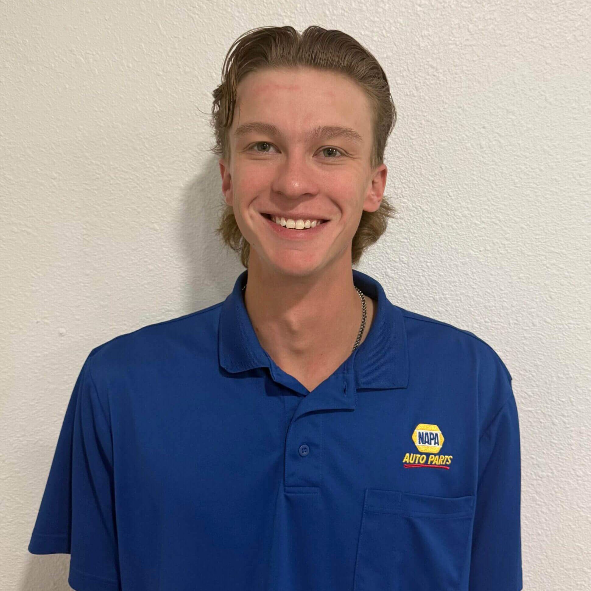 Young man smiling in a blue polo shirt with a logo.